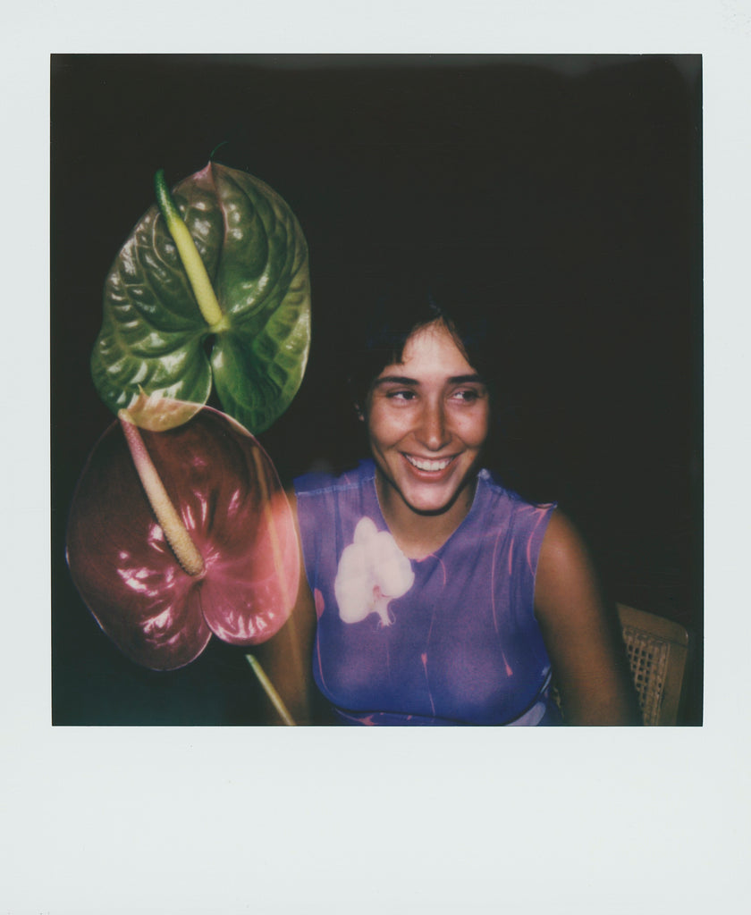 This sheer purple top with an orchid print blends organic forms with structured design, creating a harmonious contrast. The anthurium flowers add a natural, sculptural element to the composition, enhancing the raw and intimate aesthetic of the Polaroid. Capturing the fusion of nature, art, and design, the image embodies ephemeral beauty and the dialogue between fabric and the body. With an editorial storytelling approach, the visuals feel authentic, highlighting the essence of organic shapes in fashion.




