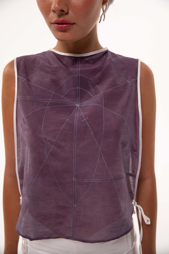 Close-up of a sheer silk top in deep violet, featuring intricate embroidered sacred geometry patterns and white trim. Ethereal, sustainable fashion blending minimalist design with mathematical precision.